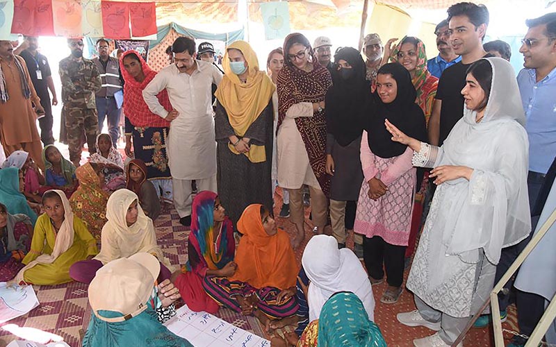 This handout picture taken and released by Chief Minister House Office of Sindh Province on October 12, 2022 shows Nobel Peace laureate Malala Yousafzai (R) speaking with flood-affected children at a makeshift school in Johi, Dadu district of Sindh province. — AFP