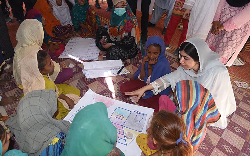 This handout picture taken and released by Chief Minister House Office of Sindh Province on October 12, 2022 shows Nobel Peace laureate Malala Yousafzai (R) speaking with flood-affected children at a makeshift school in Johi, Dadu district of Sindh province. — AFP