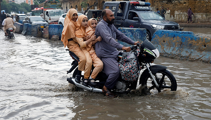 A man and students ride on a motorcycle on a flooded road, following rains during the monsoon season in Karachi, Pakistan August 10, 2022. — Reuters
