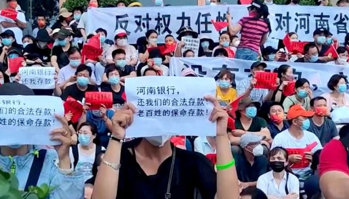 Demonstrators hold up signs during a protest over the freezing of deposits by some rural-based banks, outside a Peoples Bank of China building in Zhengzhou, Henan province, China July 10, 2022, in this screengrab from video obtained by Reuters. Text in foreground reads, Henan Bank, return to us our legal deposits! The peoples life-saving deposits!.— Reuters