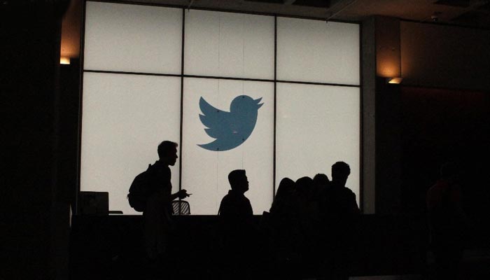 People walking in front of the Twitter logo. — AFP