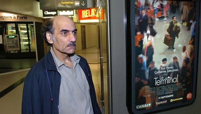 In this file photo taken on August 12, 2004, Mehran Karimi Nasseri passes by the poster of the movie inspired by his life, in terminal 1 of Paris Charles De Gaulle airport. — AFP