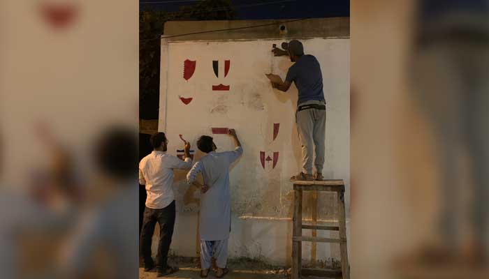 Youngsters playing football for the Gul Baloch Football Club paint a wall in their neighbourhood ahead of the FIFA World Cups beginning. — Photo by author