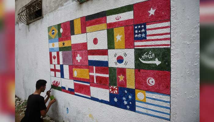 One of the residents of Malirs Siddique Goth paints a wall on the street with flags of participating countries. — Twitter/FIFA/@FIFAcom