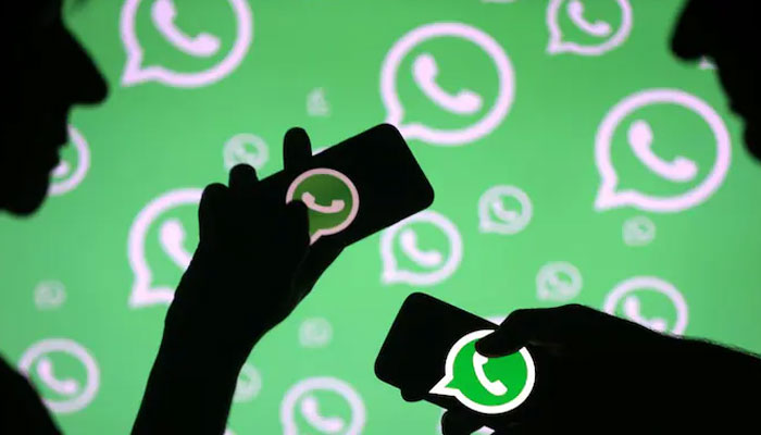 Silhouettes seen holding smartphones in front of a lighted screen showing the WhatsApp logo. — Reuters/File