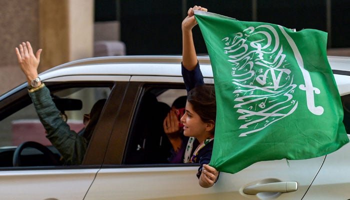 Seorang penggemar sepak bola Saudi mengibarkan bendera negara mereka dari jendela mobil di Riyadh saat merayakan setelah pertandingan sepak bola Grup C Piala Dunia Qatar 2022 antara Argentina dan Arab Saudi pada 22 November 2022. — AFP