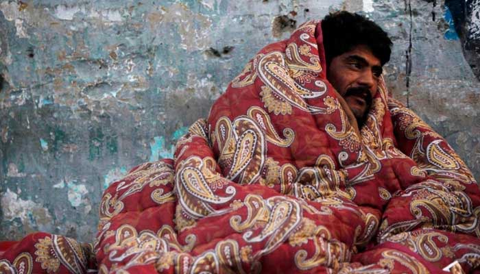 A man covers himself with a cotton blanket to stay warm during winter in the early hours of the morning near a bus stop in Karachi. — Reuters/File