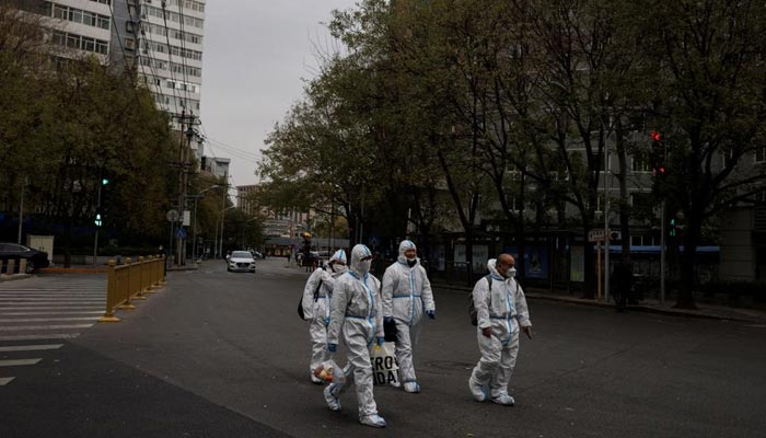 28 نومبر 2022 کو بیجنگ، چین میں کورونا وائرس کی بیماری (COVID-19) کے پھیلنے کے بعد حفاظتی سوٹ میں مرد سڑک پر چل رہے ہیں۔ - رائٹرز