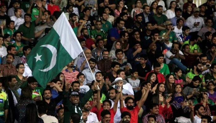 15 ستمبر 2017 کو لاہور، پاکستان میں ورلڈ الیون کرکٹ سیریز کا فائنل میچ دوسروں کے ساتھ دیکھتے ہوئے ایک تماشائی پاکستان کا قومی پرچم لہرا رہا ہے۔ — رائٹرز