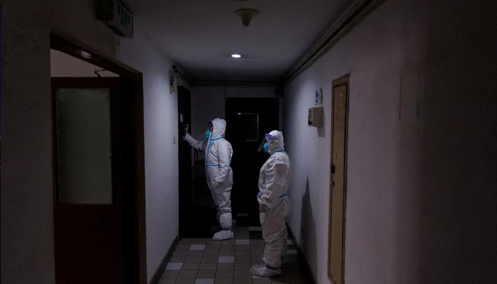 حفاظتی سوٹ میں وبائی امراض سے بچاؤ کے کارکن ایک اپارٹمنٹ کی عمارت میں رہائشیوں کے دروازے پر دستک دیتے ہیں جو لاک ڈاؤن میں چلا گیا تھا کیونکہ بیجنگ، 2 دسمبر 2022 میں کورونا وائرس کی بیماری (COVID-19) کی وباء جاری ہے۔ - رائٹرز