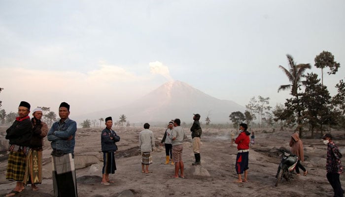Villagers stand in an area covered with volcanic ash as Mount Semeru volcano erupts volcanic materials, as seen in the background in Sumberwuluh, Lumajang, East Java province, Indonesia, December 5, 2022, in this photo taken by Antara Foto. Antara Foto/Umarul Faruq/via REUTERS