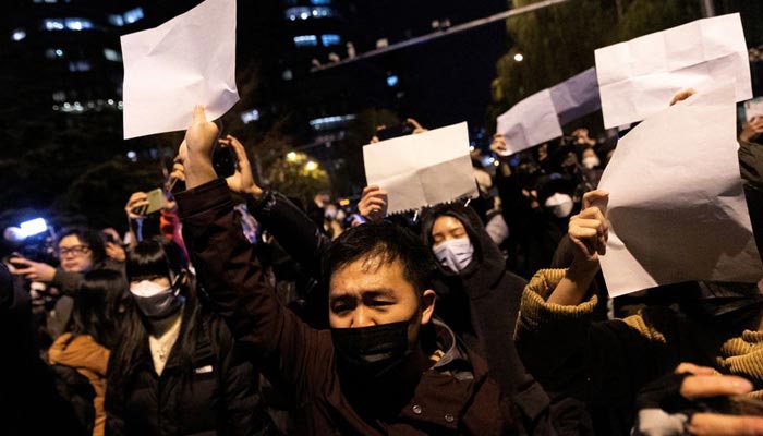 بیجنگ، چین میں، 28 نومبر، 2022 کو، اورومچی میں آگ کے متاثرین کے لیے نگرانی کے بعد، لوگ کورونا وائرس کی بیماری (COVID-19) کی پابندیوں کے خلاف احتجاج میں کاغذ کی سفید چادریں تھامے ہوئے ہیں۔