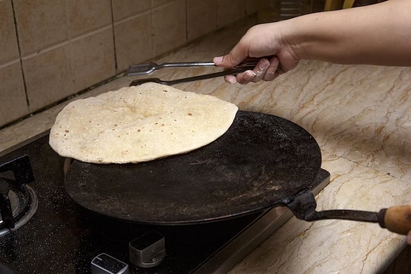 ایک عورت روایتی ککر پر روٹی (ایشیائی روٹی) پکا رہی ہے جسے توا کہتے ہیں۔— انسپلیش