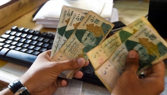A Pakistani man counts Pakistan’s rupees at his shop in Karachi. — AFP