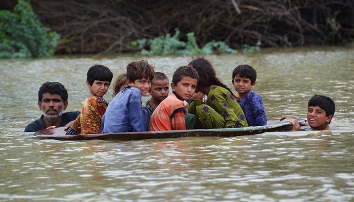 26 اگست 2022 کو صوبہ بلوچستان کے ضلع جعفرآباد میں مون سون کی شدید بارشوں کے بعد سیلاب زدہ علاقے میں ایک شخص (بائیں) ایک نوجوان کے ساتھ بچوں کو منتقل کرنے کے لیے سیٹلائٹ ڈش کا استعمال کر رہا ہے۔ — AFP