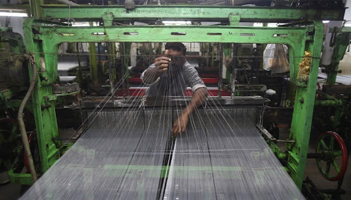 A Pakistan textile labourer fixes broken threads at a power loom in Karachi, the financial capital and the largest industrial city of Pakistan. Photo: AFP