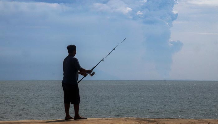 A man fishes at Pasauran beach, Anyer in Serang on April 24, 2022 while Mount Anak Krakatau spews thick smoke into the air. — AFP