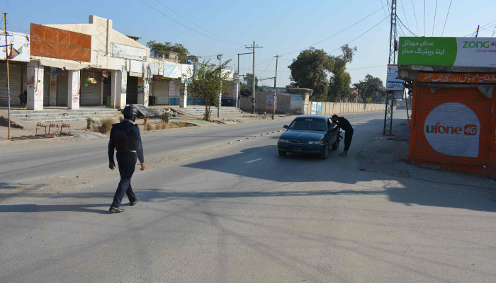 A policeman checks a car in front of a shuttered market in Bannu on December 20, 2022. — AFP