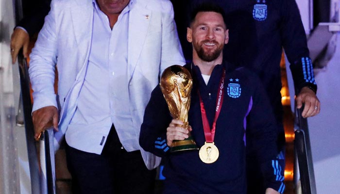 Claudio Tapia, presiden Asosiasi Sepak Bola Argentina dan Lionel Messi dengan trofi saat kedatangan tim di Bandara Internasional Ezeiza di Buenos Aires, Argentina pada 20 Desember 2022 — Reuters 