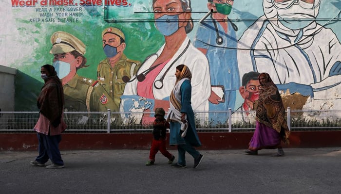 Women walk past a graffiti amidst the spread of the coronavirus disease (COVID-19) in New Delhi, India, February 7, 2022. — Reuters