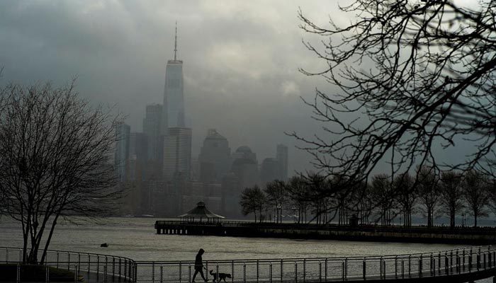 A woman walks her dog in a local park in Hoboken, New Jersey, while storm clouds pass by the One World Trade Center in New York, U.S., December 23, 2022. — Reuters