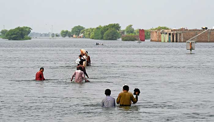 Internally displaced people wade through floodwaters to return home after heavy monsoon rains in Dadu district, Sindh province on September 7, 2022. Record monsoon rains have caused devastating floods across Pakistan since June, killing more than 1,200 people and leaving almost a third of the country under water, affecting the lives of 33 million. — AFP