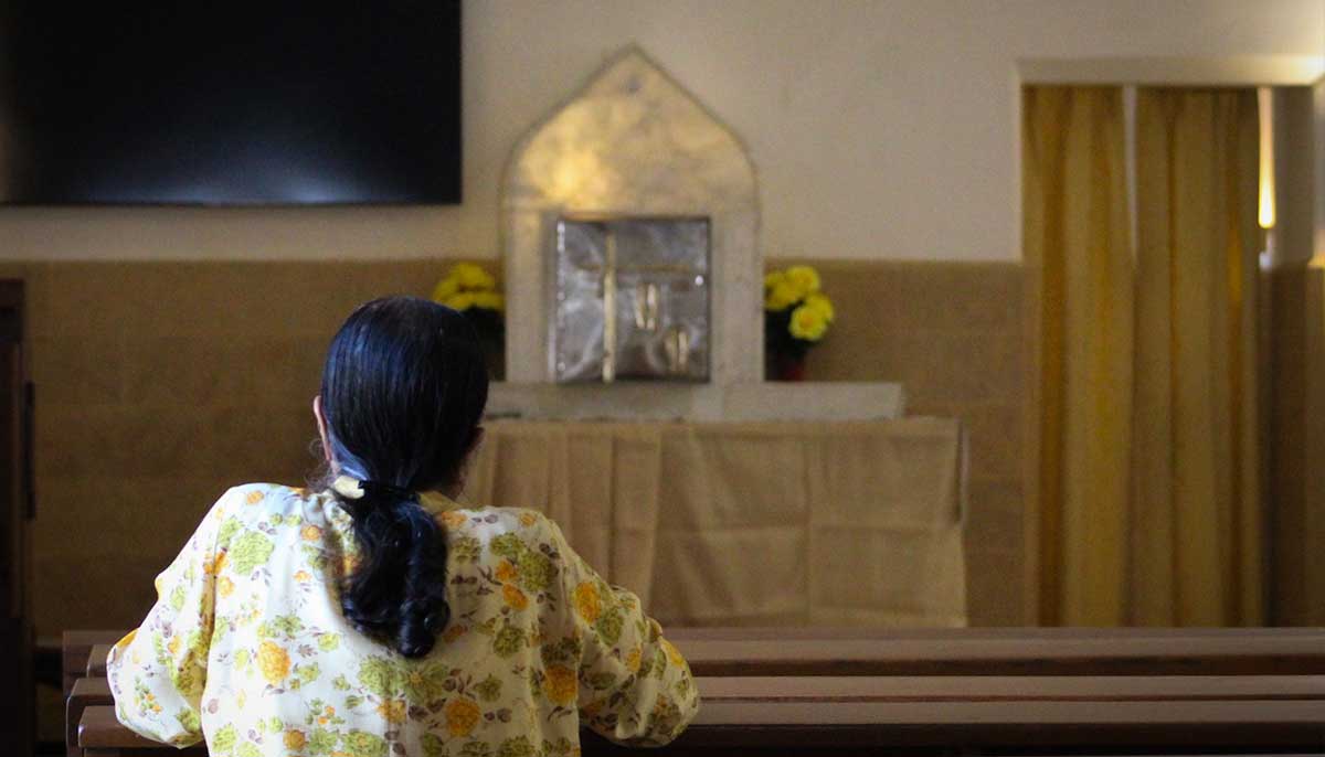 An elderly devotee sits across the blessed sacrament in the church.