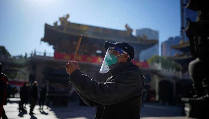 A man wearing a protective mask and face shield worships at the Buddhist Jingan Temple, December 23, 2022. — Reuters