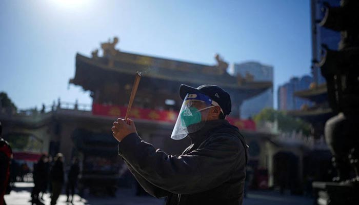 حفاظتی ماسک اور چہرے کی ڈھال پہنے ایک شخص بدھ مت کے جنگن مندر میں پوجا کر رہا ہے، کیونکہ 23 ​​دسمبر 2022 کو چین کے شہر شنگھائی میں کورونا وائرس کی بیماری (COVID-19) پھیل رہی ہے۔ - رائٹرز