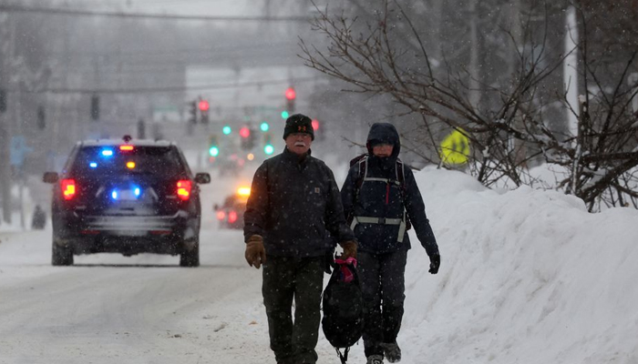 موسم سرما کے طوفان کے دوران لوگ سڑک پر چل رہے ہیں جو کہ ایمہرسٹ، نیو یارک، US، 26 دسمبر 2022 کو بفیلو کے علاقے سے ٹکرایا۔