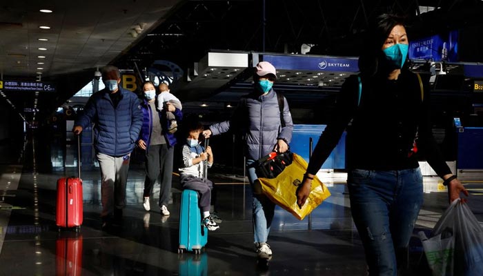 بیجنگ، چین میں 27 دسمبر 2022 کو کورونا وائرس کی بیماری (COVID-19) پھیلنے کے درمیان مسافر بیجنگ کیپیٹل انٹرنیشنل ایئرپورٹ پر اپنے سامان کے ساتھ چل رہے ہیں۔ - رائٹرز
