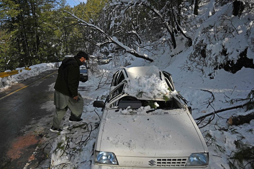 A tourist checks a damaged car stucked on a road following a blizzard that started on January 7 which led to visitors being trapped in vehicles along the roads to the resort hill town of Murree. — AFP