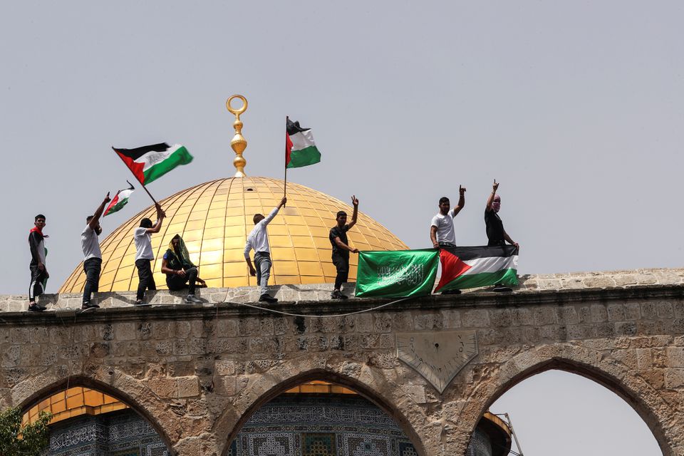 21 مئی 2021 کو یروشلم اولڈ سٹی میں فلسطینی جھنڈے اٹھائے ہوئے ہیں جب وہ مسجد اقصیٰ کے احاطے میں کھڑے ہیں، جسے مسلمانوں کے نزدیک نوبل سینکچری اور یہودیوں کے لیے ٹمپل ماؤنٹ کے نام سے جانا جاتا ہے۔— رائٹرز