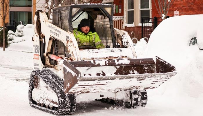 بفیلو، نیو یارک، یو ایس، 27 دسمبر، 2022 کو ایک شخص موسم سرما کے طوفان کے بعد پھنسی ہوئی کار کے ارد گرد سے برف ہٹانے کے لیے بوبکیٹ کا استعمال کر رہا ہے۔ — رائٹرز