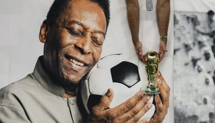 Football - FIFA World Cup Qatar 2022 - Group G - Cameroon v Brazil - Lusail Stadium, Lusail, Qatar - December 2, 2022 Brazil fan holds a replica World Cup trophy in front of a banner of Pele inside the stadium before the match. — Reuters