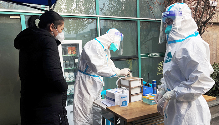 حفاظتی سوٹ میں ایک طبی کارکن 31 دسمبر 2022 کو چین کے صوبہ ہوبی کے شہر ووہان میں، کورونا وائرس کی بیماری (COVID-19) کے پھیلنے کے درمیان، ووہان کے مرکزی ہسپتال کے بخار کے کلینک کے داخلی راستے پر ایک مریض کے لیے معلومات کا اندراج کر رہا ہے۔ - رائٹرز