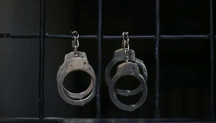 Representational image of hand cuffs hanging on prison bars. — Reuters