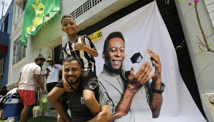 Guilherme dos Santos Malaquias, anggota dewan kota, dan putranya Gustavo dos Santos Malaquias berpose di depan bendera dengan wajah Pelé.  Penggemar Santos dapat mengucapkan selamat tinggal kepada legenda sepak bola Brasil Pele pada hari Senin.  — Reuters