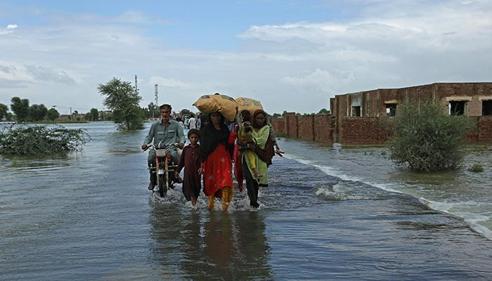 Flood victims wade through a flooded area in Rajanpur district of Punjab province on August 25, 2022. — AFP
