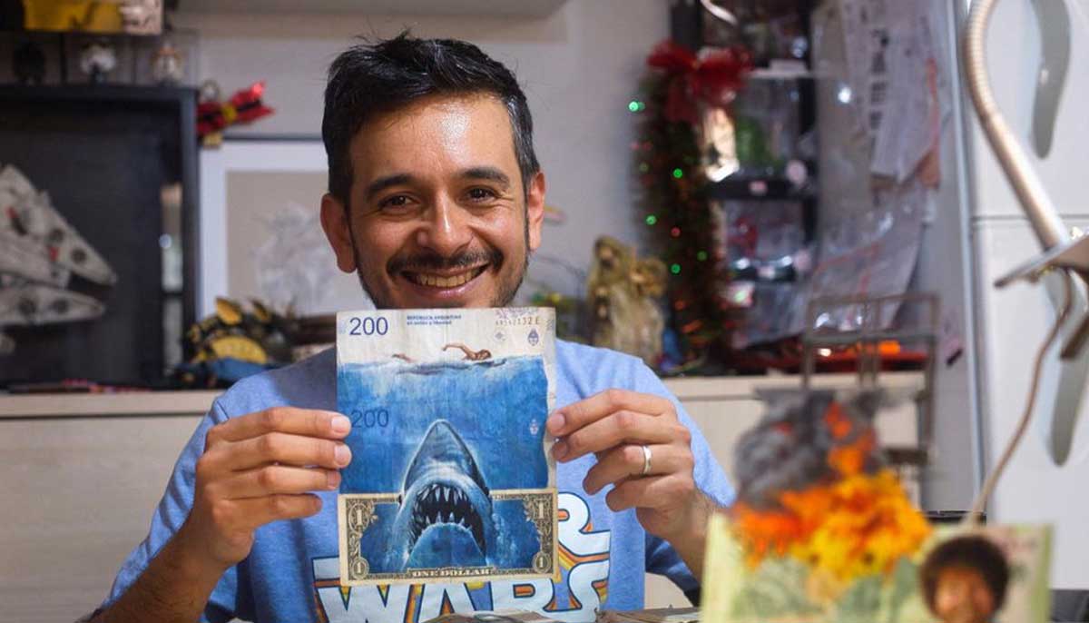 Seniman Sergio Diaz memegang uang kertas peso Argentina dan dolar AS yang menggambarkan film Shark karya Steven Spielberg sebagai parodi inflasi Argentina yang terus meningkat, di Salta, Argentina, 30 Desember 2022. — Reuters