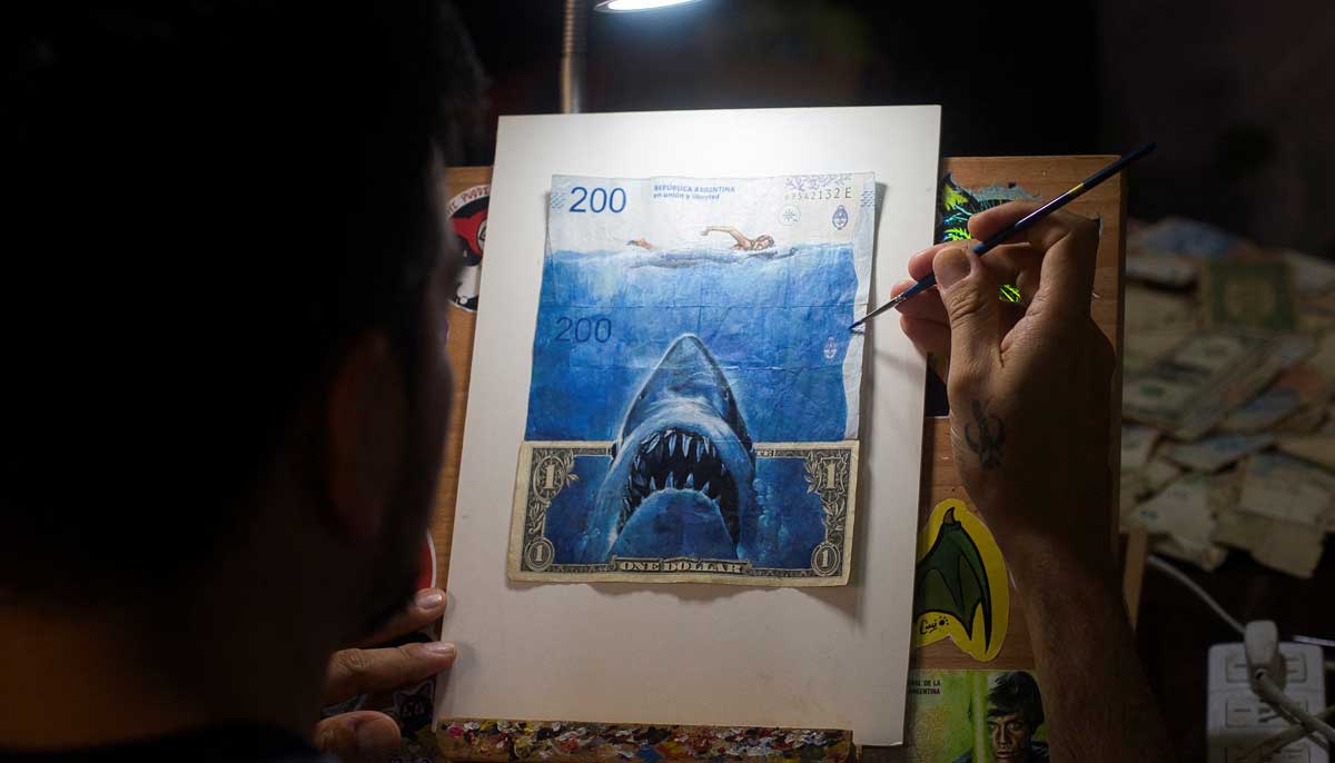 Seniman Sergio Diaz mengintervensi uang kertas peso Argentina dan uang kertas dolar AS yang menggambarkan film Shark karya Steven Spielberg sebagai parodi inflasi Argentina yang terus meningkat, di Salta, Argentina, 30 Desember 2022. — Reuters