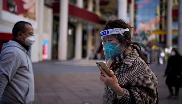 Seorang wanita yang mengenakan masker pelindung dan pelindung wajah berjalan di sepanjang distrik perbelanjaan saat China kembali bekerja meskipun wabah penyakit virus corona (COVID-19) terus berlanjut di Shanghai, China, 3 Januari 2023. — Reuters