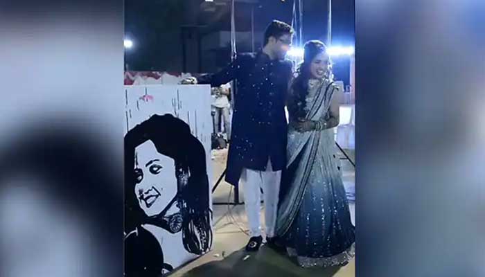 The groom and bride stand next to the latters portrait during their wedding function. — Screengrab via video/Instagram/varun.jarsania