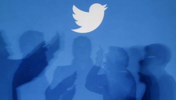 The shadows of people holding mobile phones are cast onto a backdrop projected with the Twitter logo in this illustration picture taken in Warsaw September 27, 2013. — Reuters/File