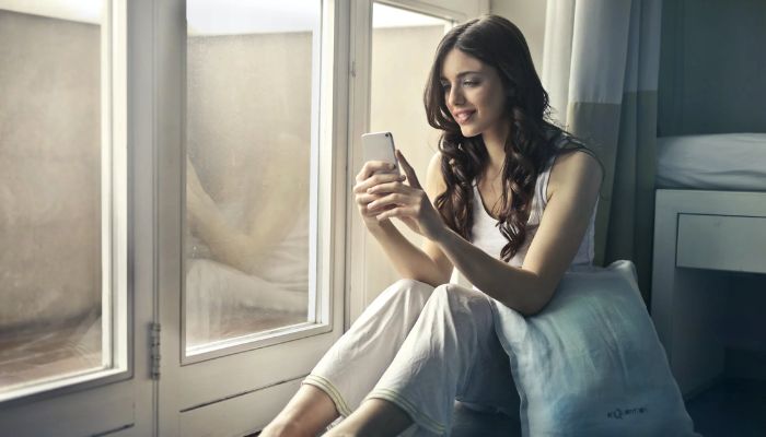 A woman sitting by the window, using a smartphone.— Pexels