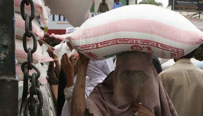 A woman carries a bag of wheat flour after buying it from a utility store in Peshawar. —Reuters/File