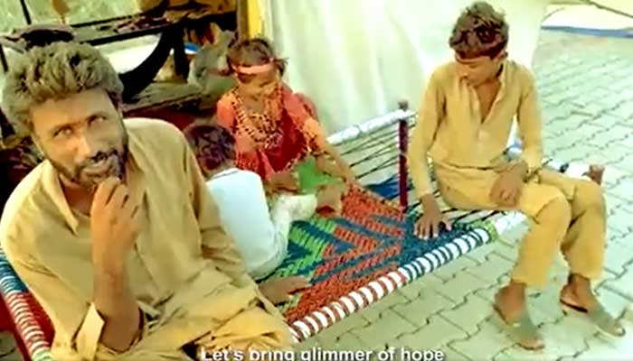 Screengrab of a sequence from the songs video showing a flood affectee seated on a charpoy with his children. — Twitter/ForeignOfficePk