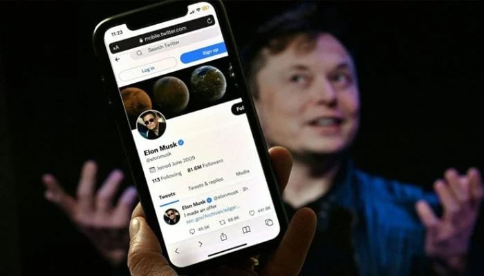 A user holds up a phone with Elon Musks Twitter profile visible against Musk. — AFP/Files