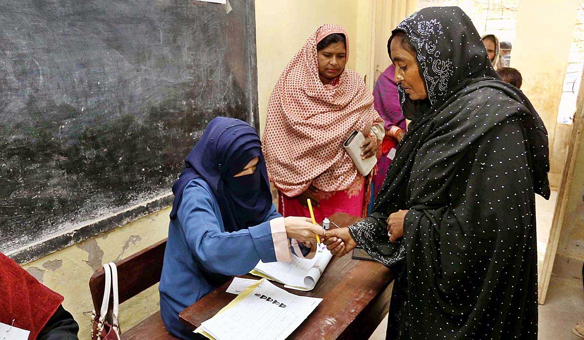 An official marks the thumb of a woman at a polling station during Local Government Elections. — APP