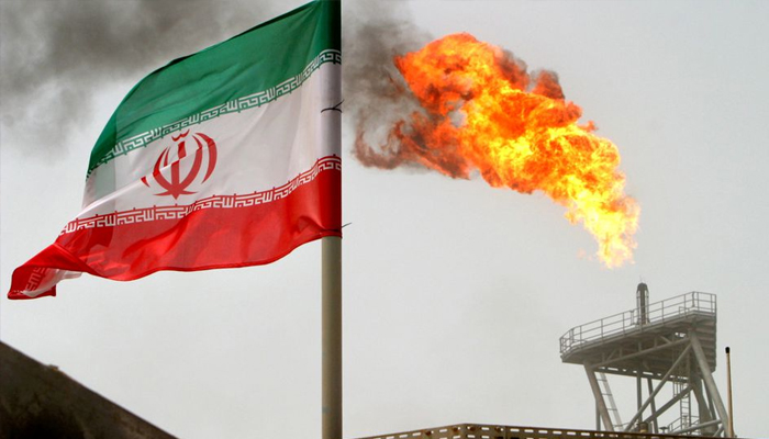 An Iranian flag is seen next to a gas flare on an oil production platform in the Gulf on July 25, 2005. — Reuters